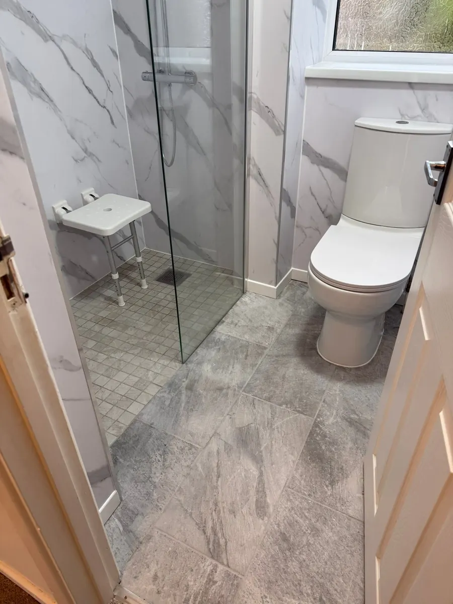 Accessible wet room with level-access mosaic shower floor, folding seat and marble-effect wall panels