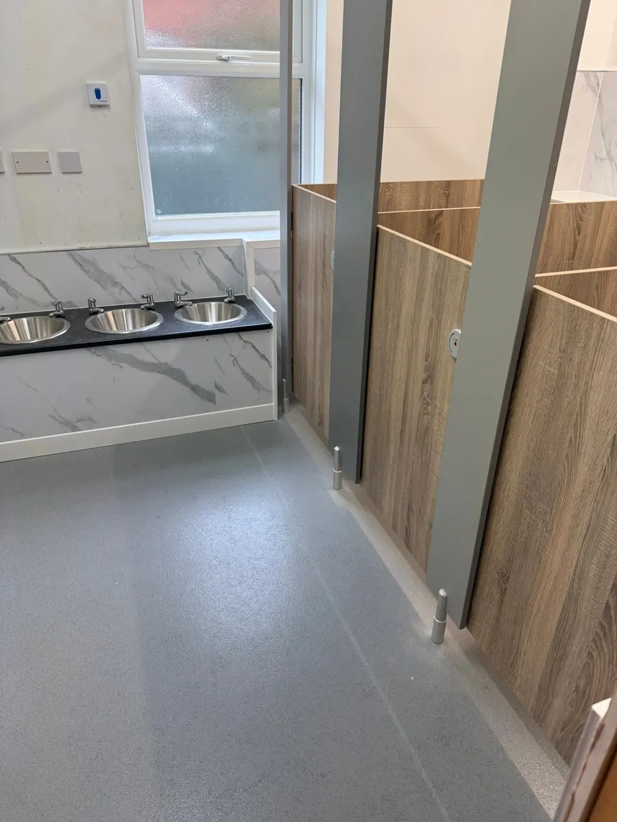 Commercial washroom fit-out with stainless steel inset basins, marble-effect trough surround and cubicles