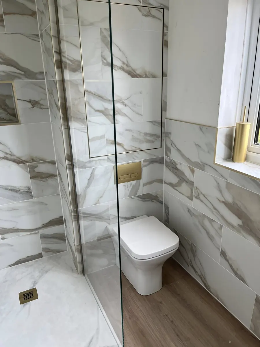 Calacatta marble-effect tiled shower room with brushed gold flush plate, drain and recessed shelf
